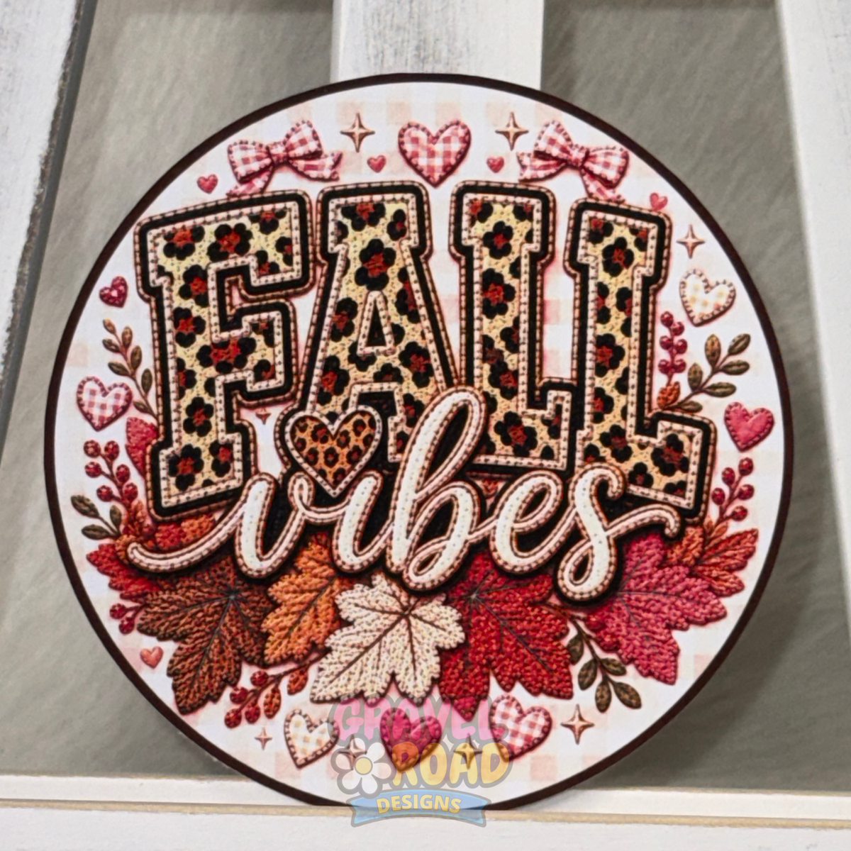 Round fall cardstock featuring leopard-print lettering, colorful autumn leaves, bows, hearts, and the phrase “Fall Vibes.” In a faux quilted pattern.