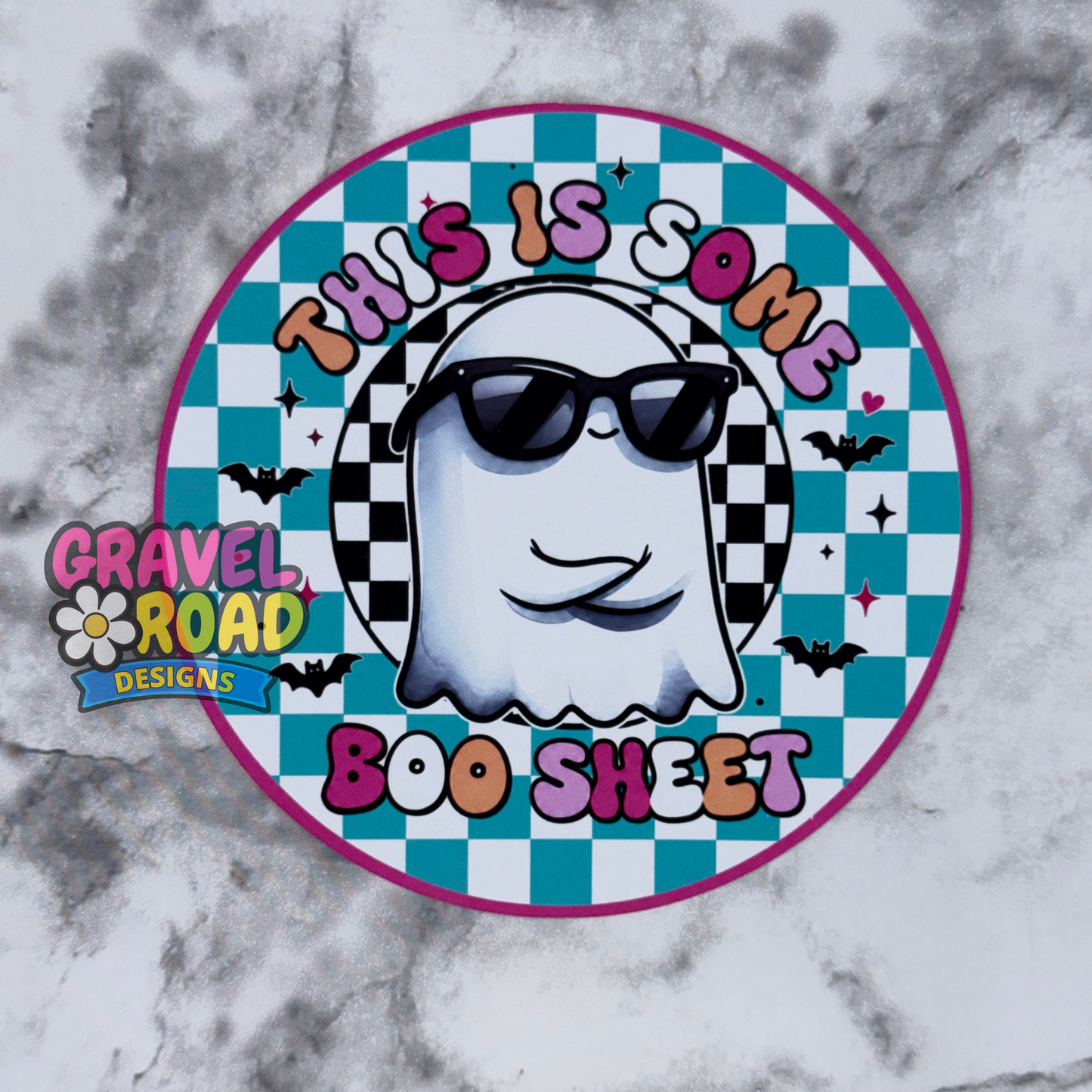 A circular cardstock design featuring a white ghost wearing black sunglasses on a teal and black checkered background, with the text 'THIS IS SOME BOO SHEET' in colorful letters. A 'Gravel Road Designs' logo is visible on the left side.