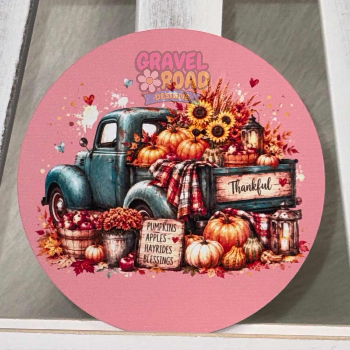 Round pink fall cardstock featuring a vintage teal truck filled with pumpkins, sunflowers, apples, plaid blankets, and a “Thankful” sign.