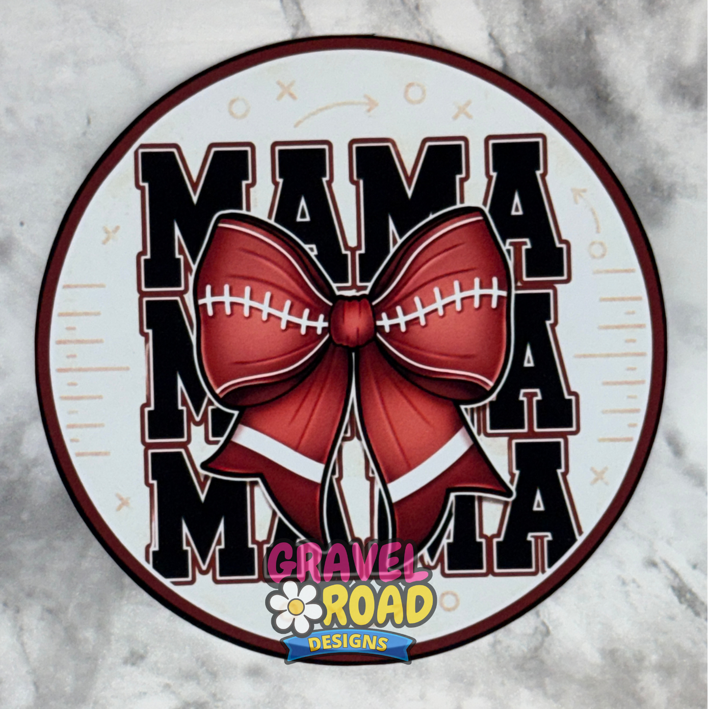 A circular cardstock design featuring the text 'MAMA' repeated vertically in black varsity-style letters with white outlines, overlaid with a large brown football bow with white laces. A 'Gravel Road Designs' logo is visible at the bottom center.