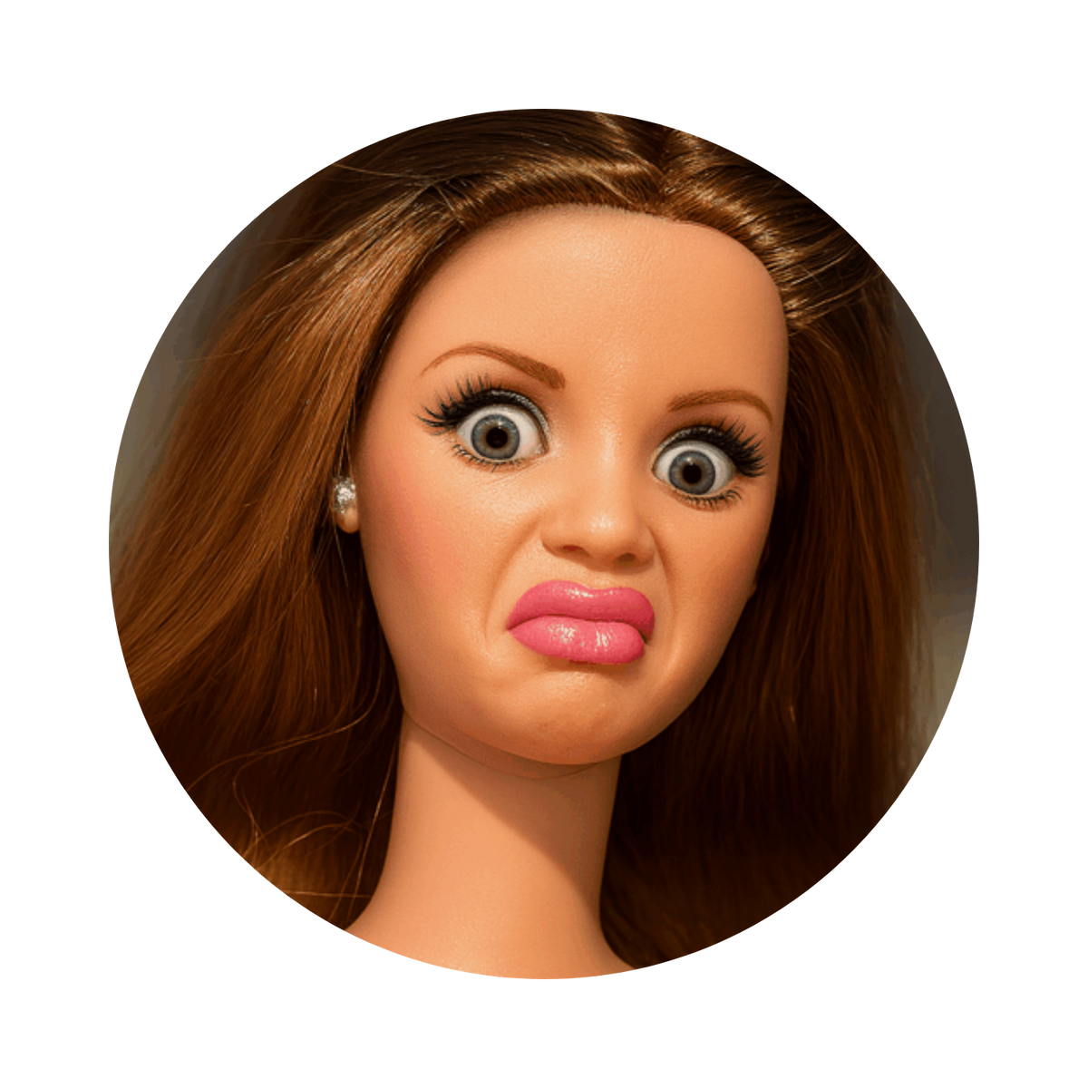 A close-up circular portrait of a doll or toy head with brown hair, large expressive eyes, and pink lips, shown on a plain white background.