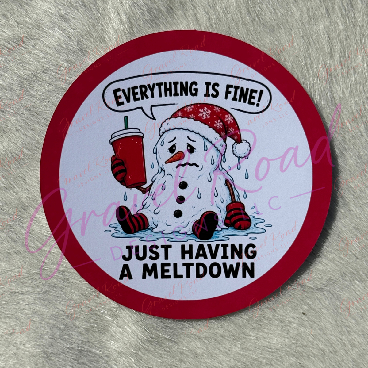 A circular cardstock with a red border and a cartoon snowman holding a red drink, with the text 'EVERYTHING IS FINE! JUST HAVING A MELTDOWN' on a gray faux-fur background.