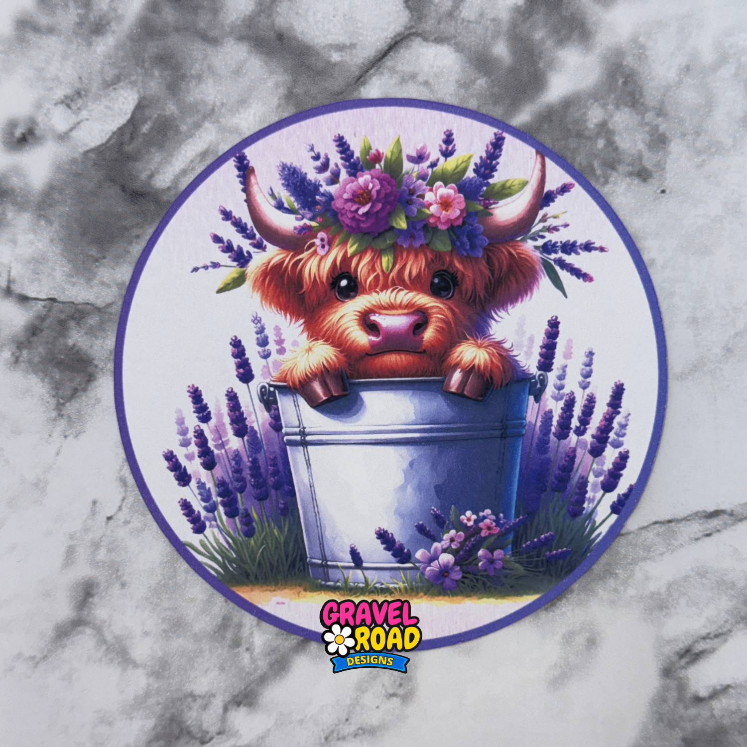 Circular printed cardstock with a cartoon Highland cow wearing a floral crown on a marble background. Gravel Road Designs logo on the bottom.