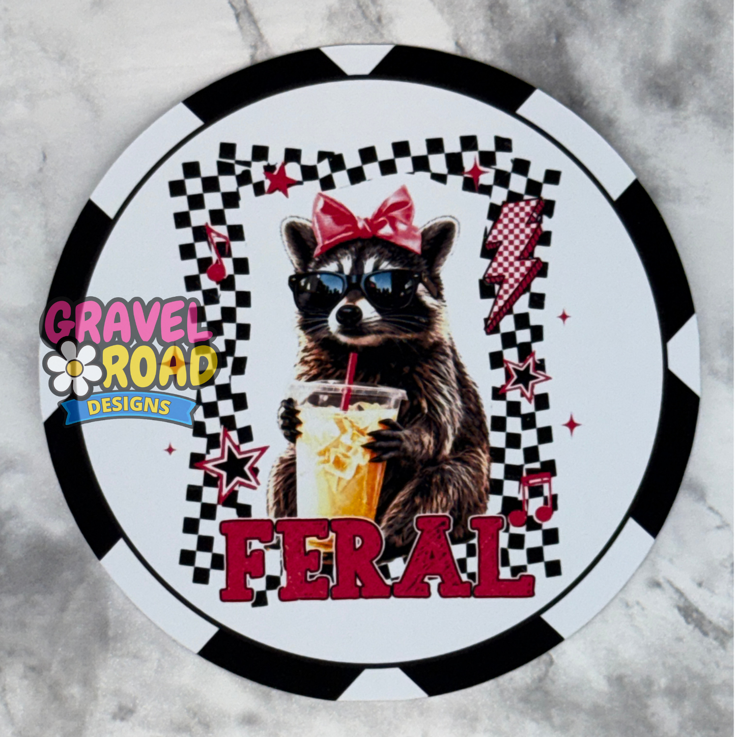 A circular cardstock design featuring a raccoon wearing sunglasses and a red bow, holding an iced drink. The design includes a black and white checkered border, red lightning bolts, stars, and the word 'FERAL' in large red letters.