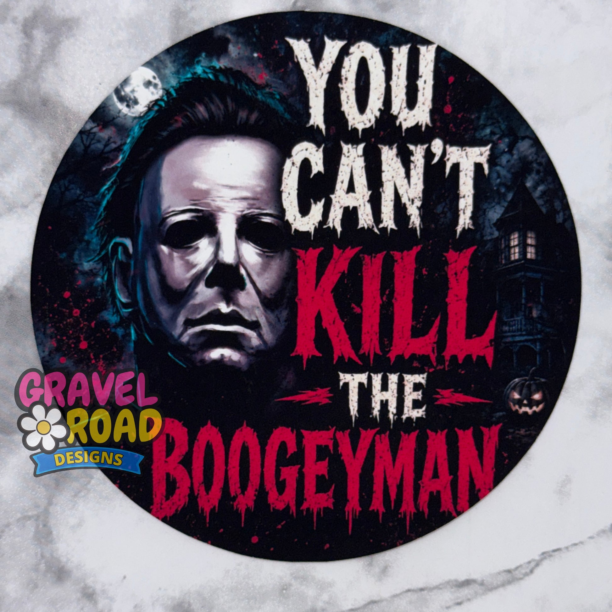 A circular Halloween-themed cardstock design featuring a grayscale portrait of Michael Myers with the text 'YOU CAN'T KILL THE BOOGEYMAN' in white and dripping red lettering. The design includes a haunted house, moon, and small jack-o'-lantern, with a 'Gravel Road Designs' logo in the lower-left corner. On a grey marble background.