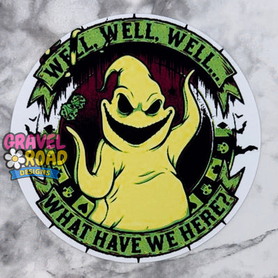A circular cardstock featuring a yellow ghost with the text "WELL WELL WELL WHAT HAVE WE HERE?" The logo Gravel Road Designs on the left-hand side. On a grey marble backdrop.