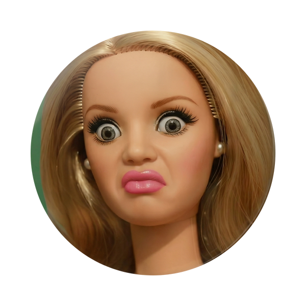 A circular close-up of a blonde doll or mannequin head with wide eyes, pink lips, and pearl earrings on a plain white background.