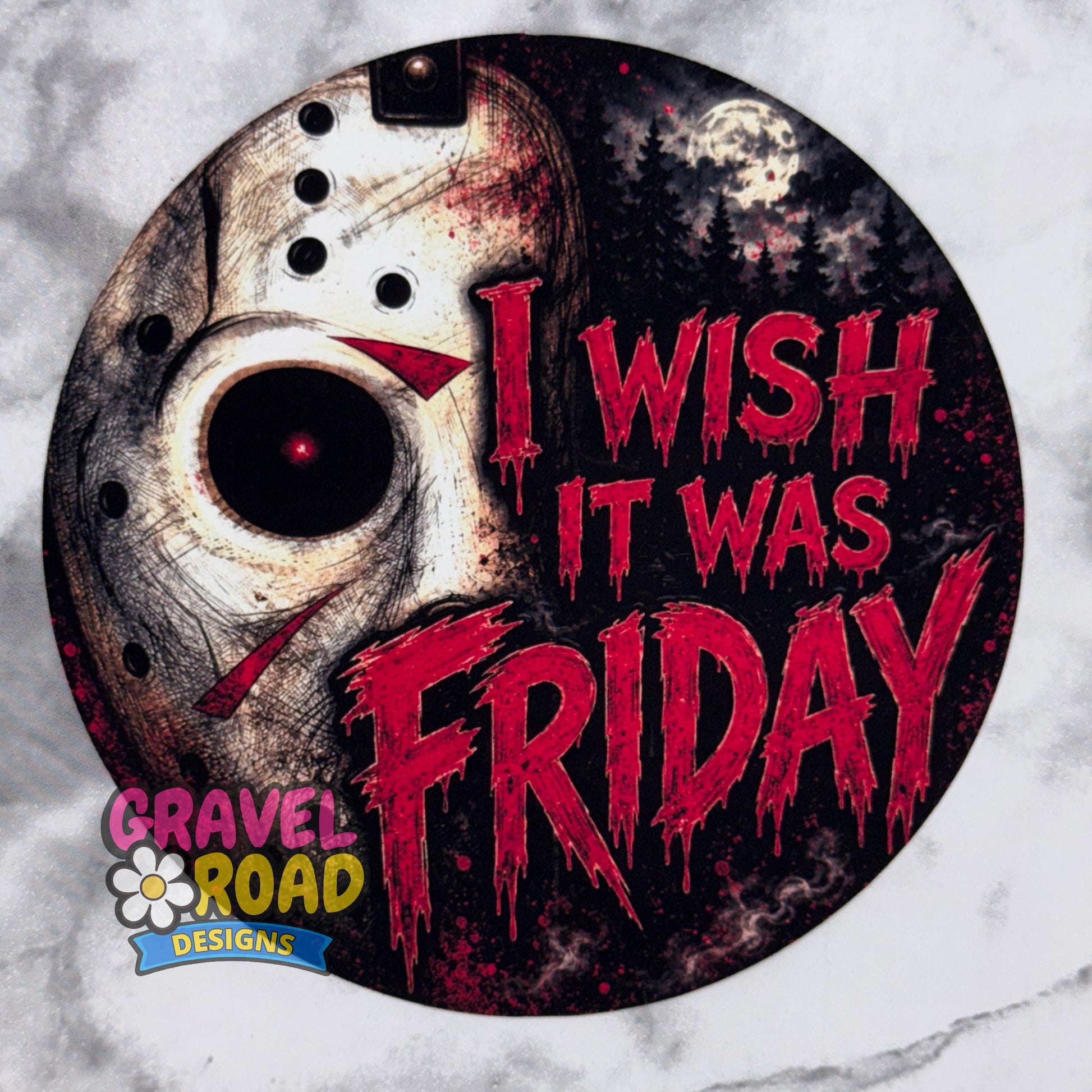 A circular cardstock featuring a distressed hockey mask on the left and the phrase 'I WISH IT WAS FRIDAY' in dripping red letters on a dark night-sky background. The design includes the Gravel Road Designs logo in the lower-left corner and is shown on a light marble-like surface.