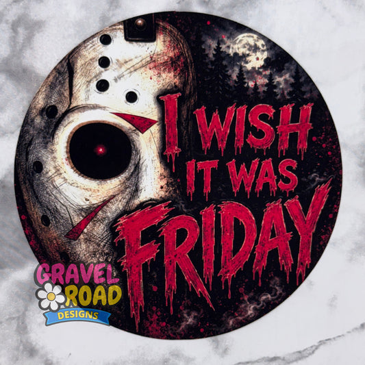 A circular cardstock featuring a distressed hockey mask on the left and the phrase 'I WISH IT WAS FRIDAY' in dripping red letters on a dark night-sky background. The design includes the Gravel Road Designs logo in the lower-left corner and is shown on a light marble-like surface.