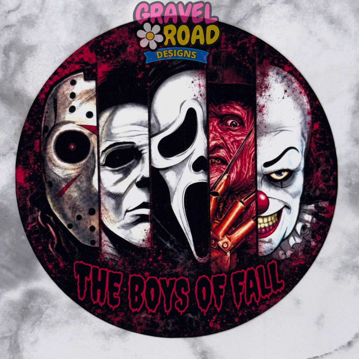 A circular cardstock featuring four horror movie masks in vertical panels: Jason Voorhees, Michael Myers, Ghostface, and Freddy Krueger, with the text 'THE BOYS OF FALL' at the bottom. The top has a 'Gravel Road Designs' logo, and the background is a light gray marbled texture.