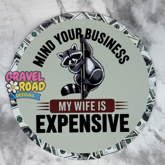 A round cardstock with a raccoon climbing a pole and the text 'MIND YOUR BUSINESS MY WIFE IS EXPENSIVE' on a green background, with a dollar bill pattern around the border and a 'Gravel Road Designs' logo on the left.