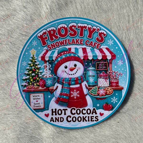 A round cardstock for 'Frosty's Snowflake Cafe' featuring a snowman at a hot cocoa stand, with the text 'Hot Cocoa and Cookies,' photographed on a gray furry surface.