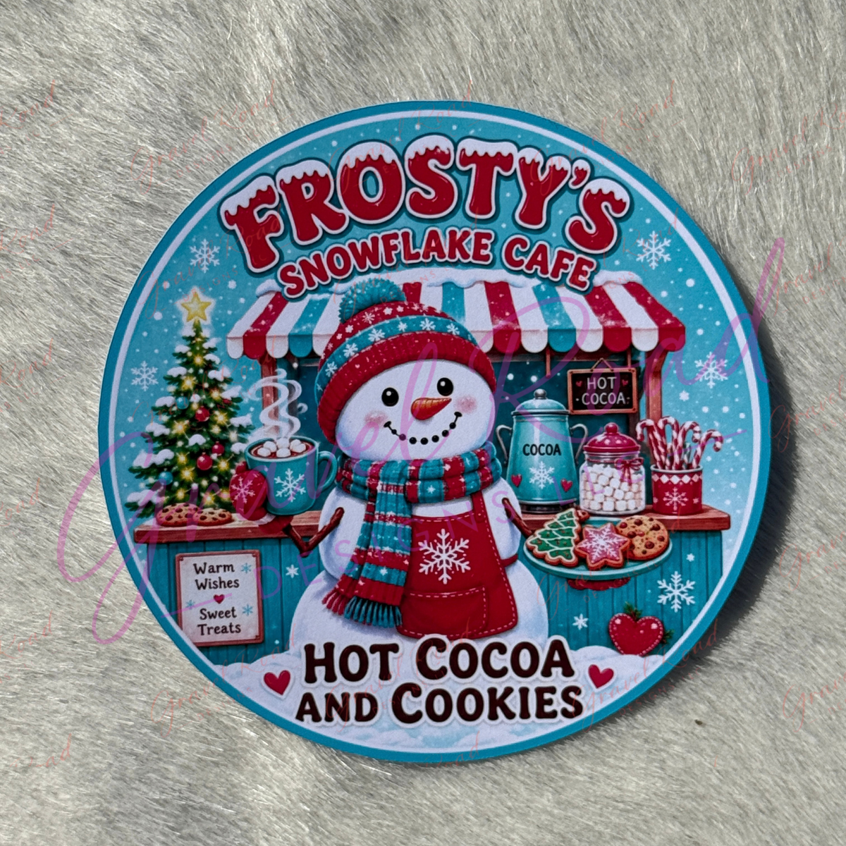 A round cardstock for 'Frosty's Snowflake Cafe' featuring a snowman at a hot cocoa stand, with the text 'Hot Cocoa and Cookies,' photographed on a gray furry surface.