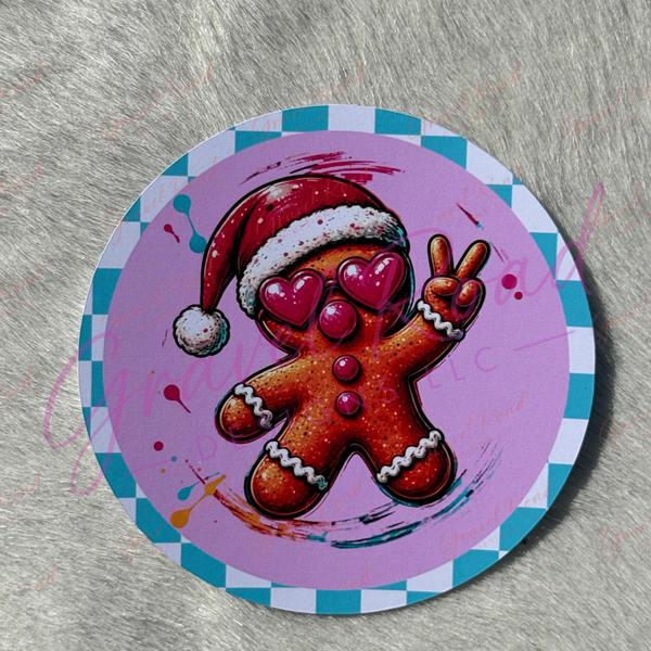 A round printed cardstock featuring a festive gingerbread figure wearing a Santa hat and heart-shaped sunglasses, making a peace sign. The design has a pink background with a blue and white checkered border, displayed against a gray textured background.