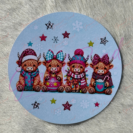 A round cardstock featuring four cute Highland cows in winter clothing, displayed on a textured gray surface.