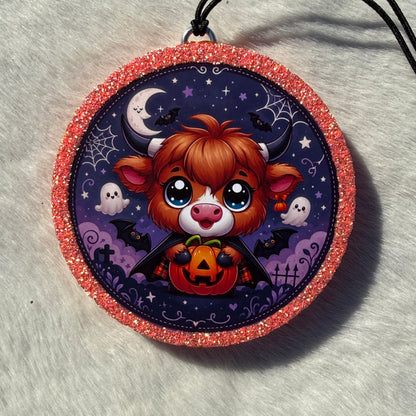 Cute Halloween Highland cow freshie with a glittery pink border, black hanging cord, and a spooky purple background featuring stars, bats, ghosts, spider webs, and gravestones.