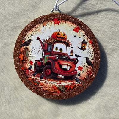 Cartoon tow‑truck fall freshie with a glittery brown border, hanging cord, pumpkins, lanterns, and autumn leaves in a seasonal Halloween scene.