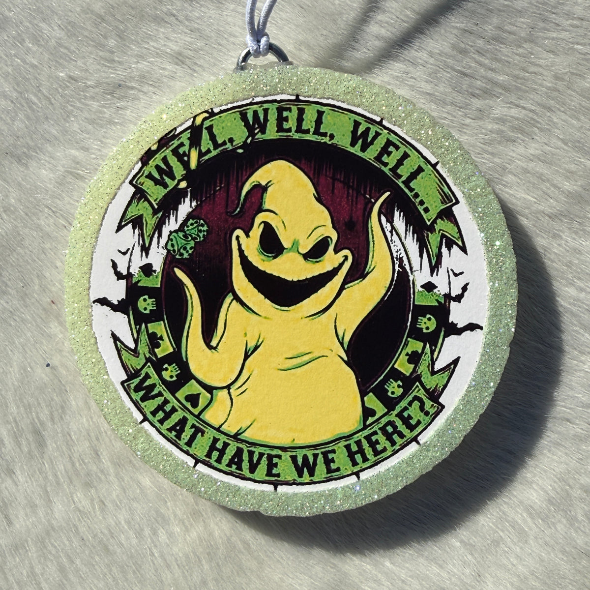 A round glittery light green and white car freshie featuring a cartoon ghost character in the center with the text 'WELL, WELL, WELL...WHAT HAVE WE HERE?"