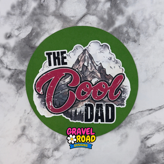 Round green cardstock with 'The Cool Dad' text and mountain graphic on a marble background