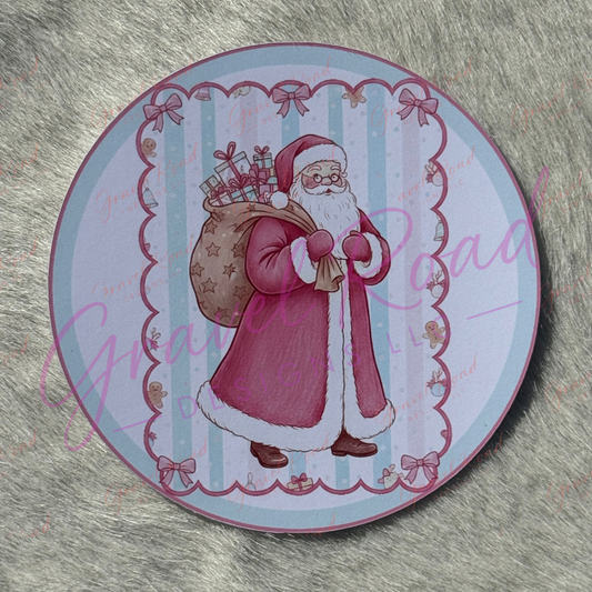 A classic Santa Claus in a red coat with white fur trim carries a large sack filled with wrapped gifts, standing against a light blue striped background with a scalloped border decorated with bows and gingerbread figures. Displayed on faux fur background.