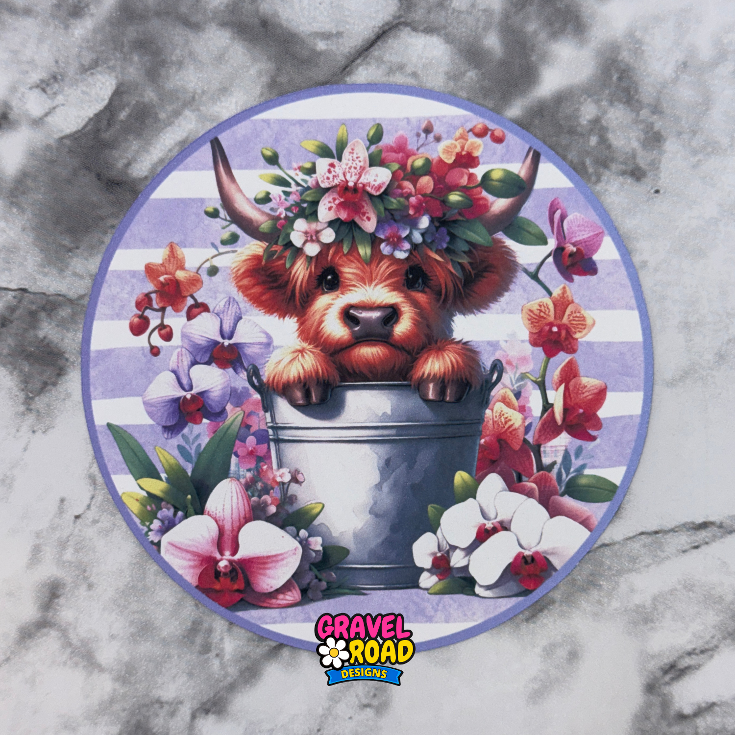Circular design with a cow in a bucket surrounded by flowers on a marble background, featuring the Gravel Road Designs logo.
