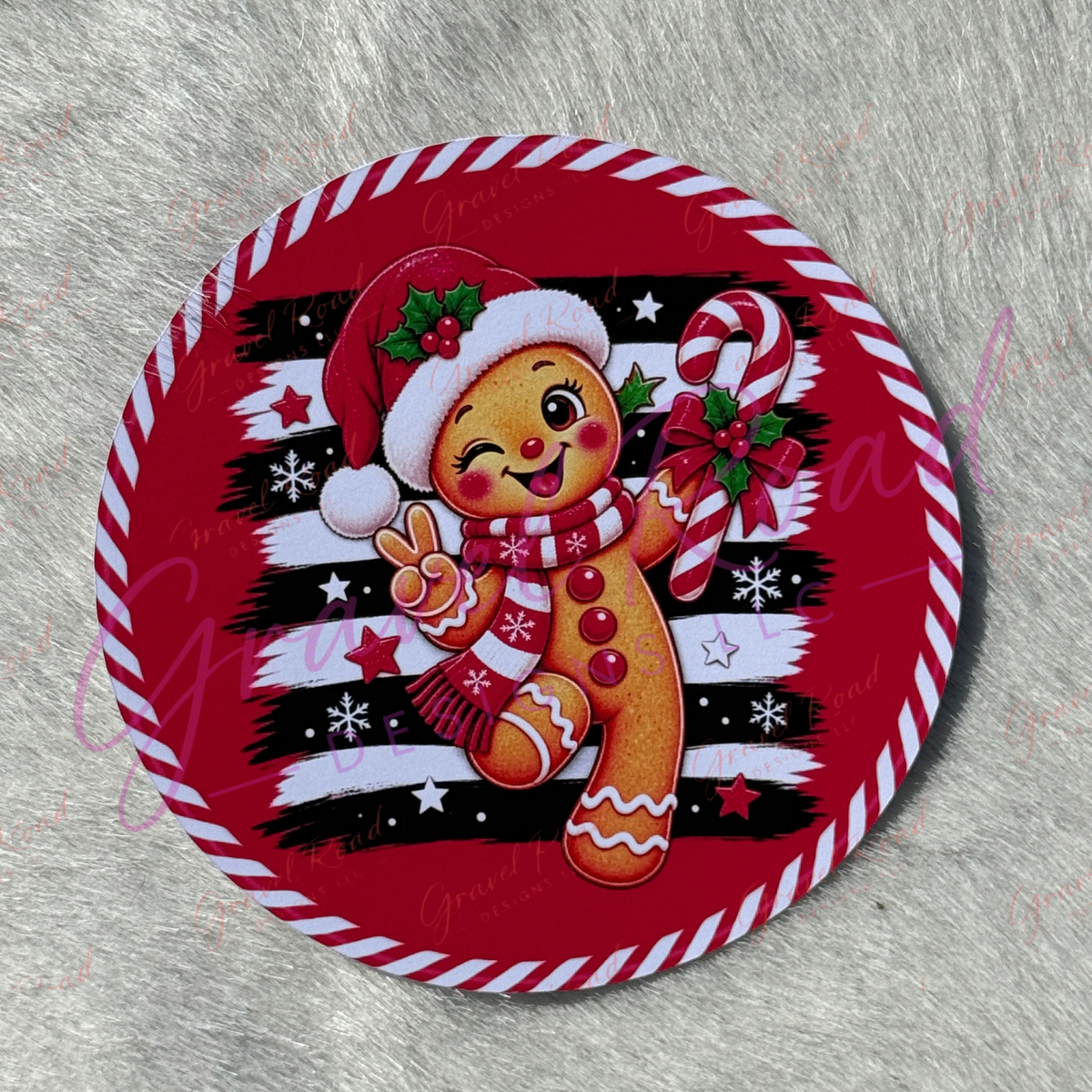 A round Christmas-themed cardstock featuring a winking gingerbread man in a red Santa hat and scarf, holding a candy cane, on a red, black, and white striped background with a red-and-white striped border. Displayed on a faux fur background.