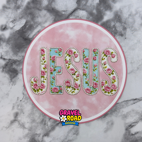Circular deep pink printed cardstock with the word “Jesus”. The sticker is photographed on a gray and white marble background, with a “Gravel Road Designs” watermark at the bottom.