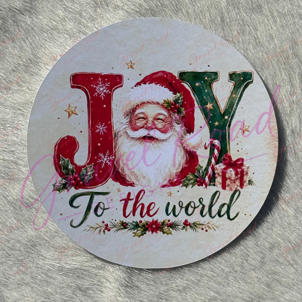 A festive Christmas cardstock design featuring the word “JOY,” with the letter O replaced by Santa Claus’s face in a red hat. The J is decorated with snowflakes and holly, and the Y is green with stars, a candy cane, and a gift box beside it. Below the word, the phrase “To the world” appears in elegant green script surrounded by holly and red berries. Displayed on a faux fur background.