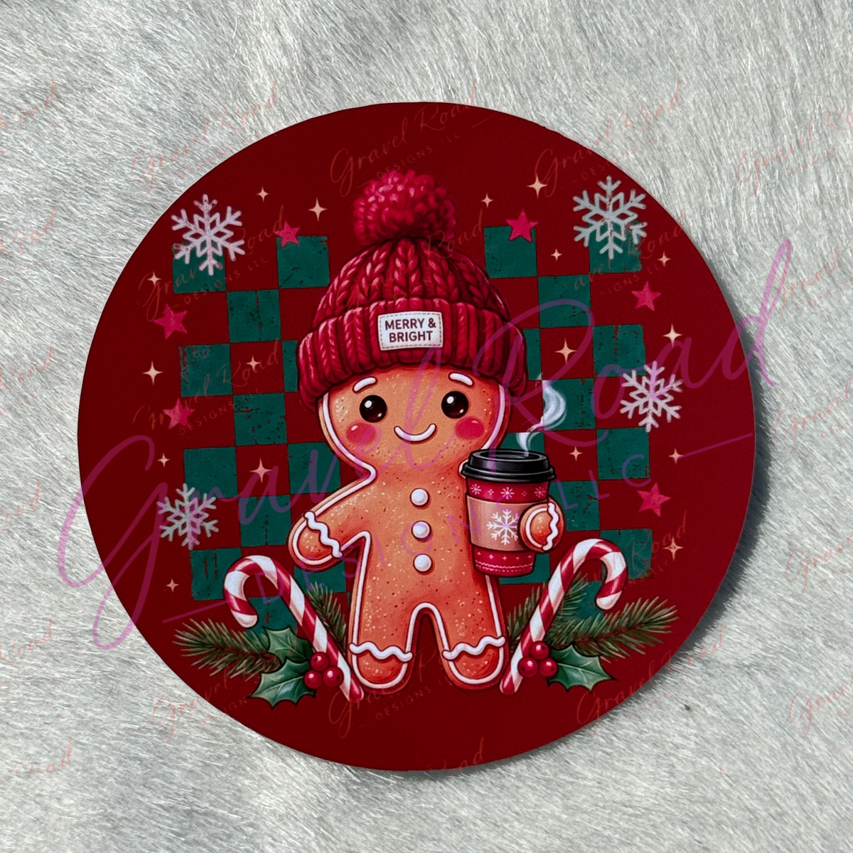 A round Christmas-themed cardstock featuring a gingerbread man wearing a red knit hat and holding a mug, surrounded by candy canes, snowflakes, and a red-and-green checkered background. Displayed on a gray textured surface.