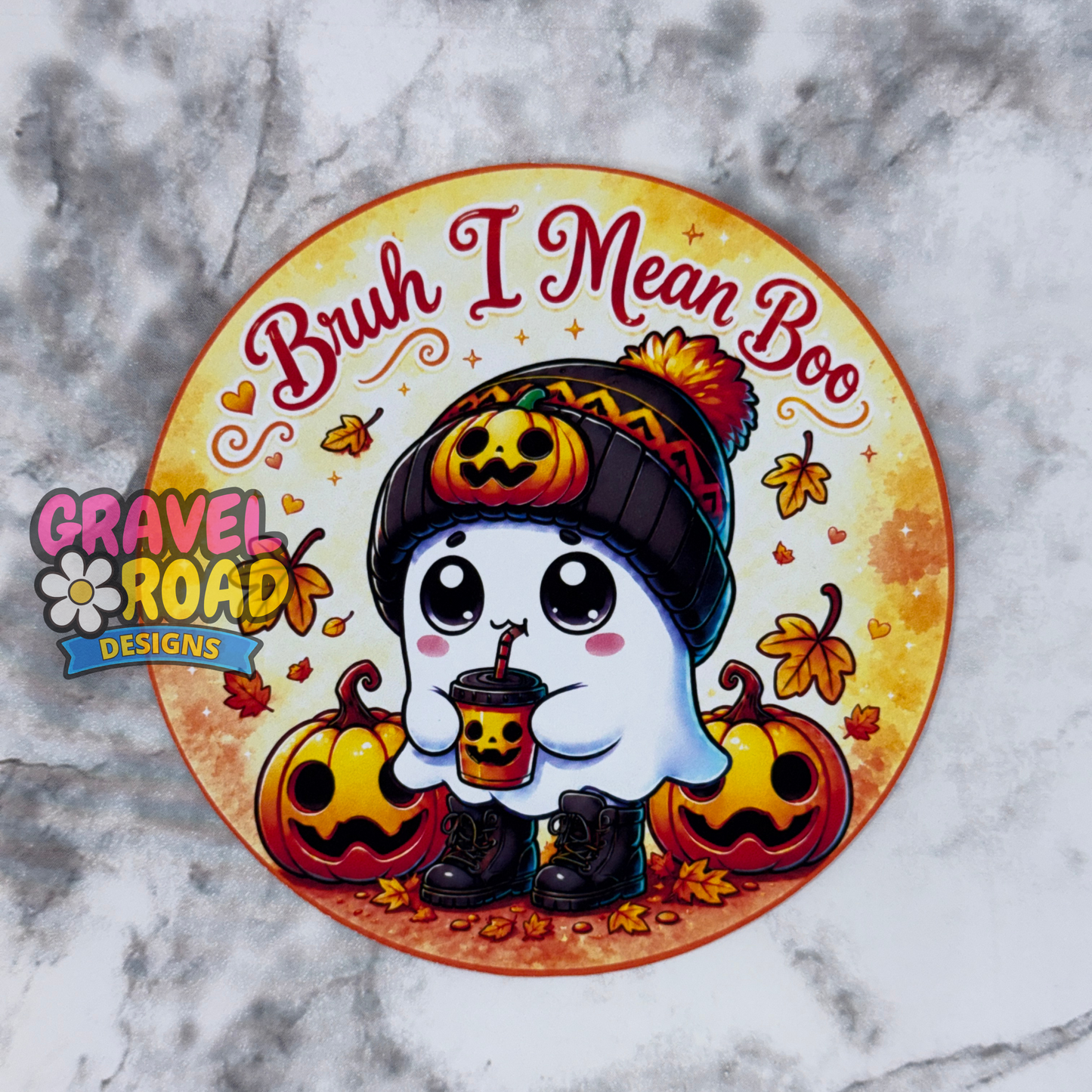 Round fall-themed freshie cardstock design featuring a cute white ghost wearing a black knit hat with a jack-o’-lantern on it, holding a pumpkin drink, and standing between two smiling pumpkins. The top text reads “Bruh I Mean Boo” in red script lettering. The background is warm yellow and orange with autumn leaves, tiny hearts, stars, and fall accents. A Gravel Road Designs watermark appears on the left side