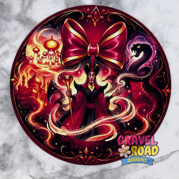 A circular cardstock featuring a stylized dark magician or sorcerer surrounded by magical swirls, a large red bow, a serpent, and fantasy castle imagery. The design is presented on a light gray marble-textured background with a 'Gravel Road Designs' logo in the bottom right corner.