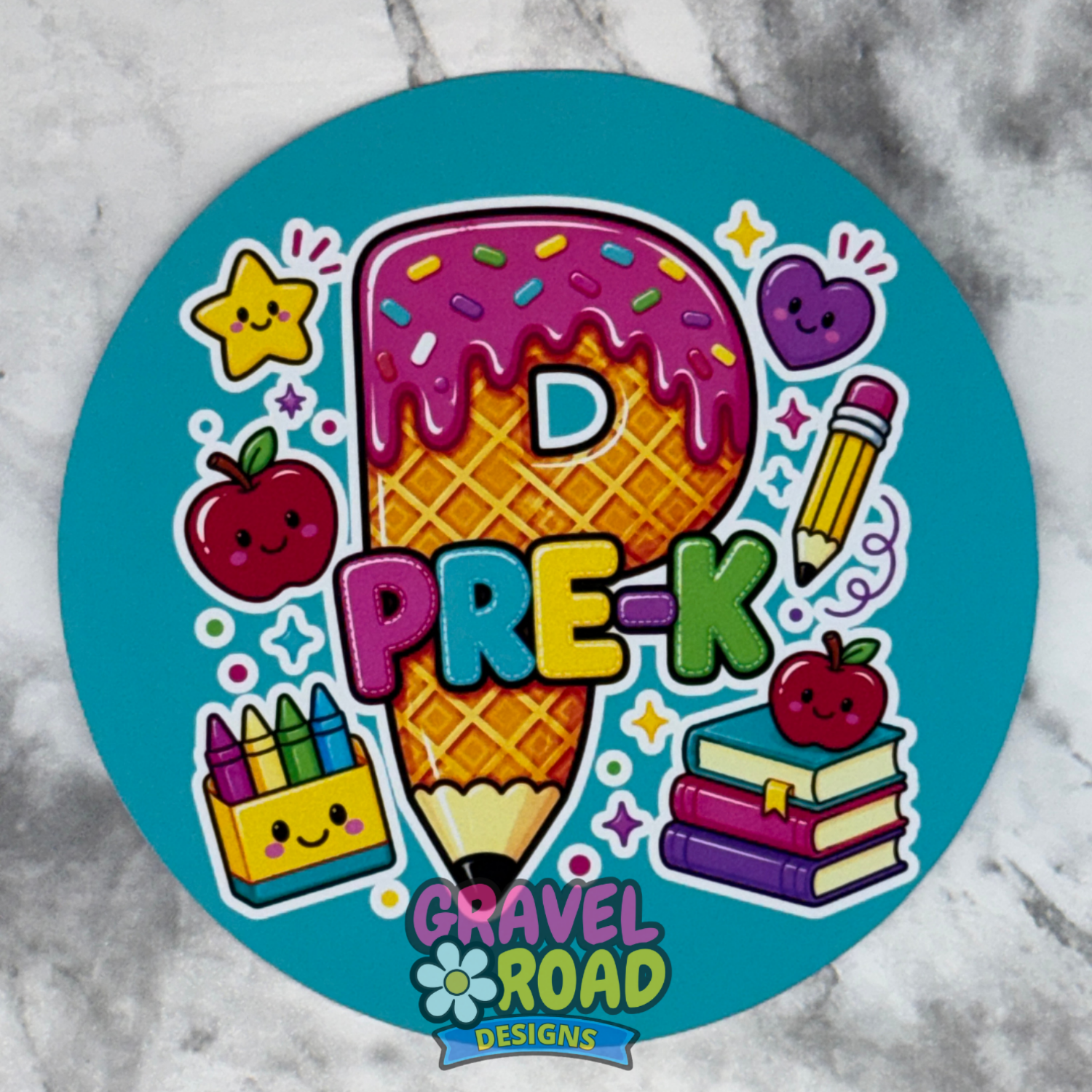 A round turquoise cardstock featuring a colorful cartoon design with the text 'PRE-K' over a waffle-cone pencil, surrounded by playful school-themed illustrations including apples, a star, a heart, a pencil, crayons, books, and the brand logo 'Gravel Road Designs' at the bottom.