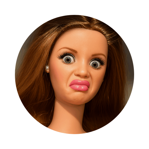 A close-up circular portrait of a doll or toy head with brown hair, large expressive eyes, and pink lips, shown on a plain white background.