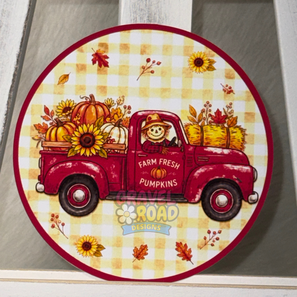 Round cardstock featuring a red vintage pickup truck loaded with pumpkins, sunflowers, and hay bales on a yellow-and-white gingham background, with the text 'FARM FRESH PUMPKINS' and a 'Gravel Road Designs' logo.
