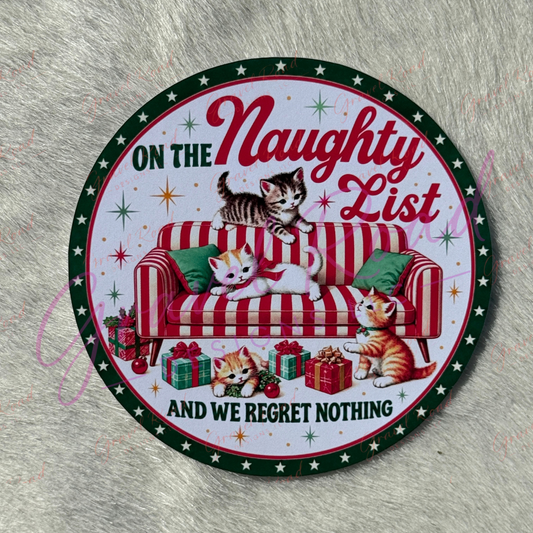A round printed cardstock featuring a festive Christmas design with three kittens on a red-and-white striped sofa, wrapped gifts, and the text 'ON THE Naughty List AND WE REGRET NOTHING' on a gray faux-fur background.