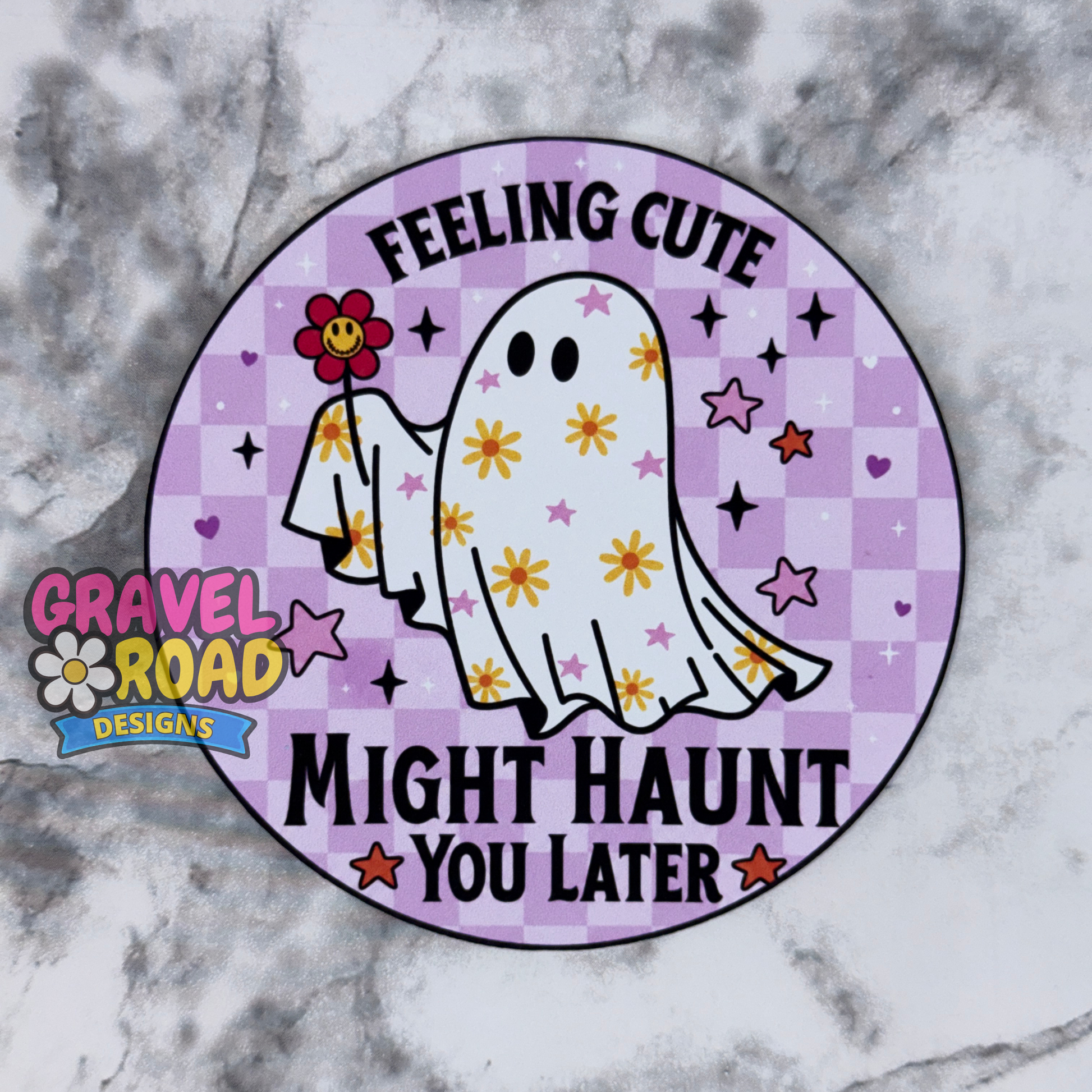 A circular cardstock with a purple checkered background, a cartoon ghost holding a flower, and the text 'FEELING CUTE MIGHT HAUNT YOU LATER.' A Gravel Road Designs logo appears on the left side.