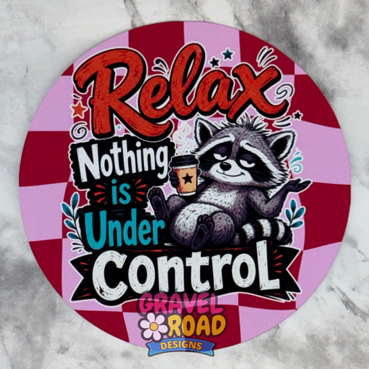 Round pink-and-red checkered cardstock design featuring a relaxed raccoon holding a coffee cup and the phrase “Relax, Nothing Is Under Control.” The logo "Gravel Road Designs" is on the bottom.