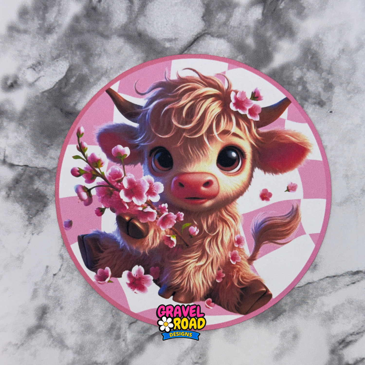 Circular printed cardstock with a cartoon Highland cow, holding flowers on a marble background. Gravel Road Designs logo on the bottom.