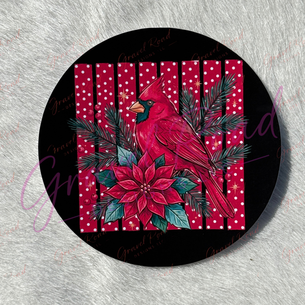 A round cardstock featuring a festive holiday design with a red cardinal, red poinsettia, green pine branches, and a red-and-white polka dot stripes, photographed on a light gray textured surface.
