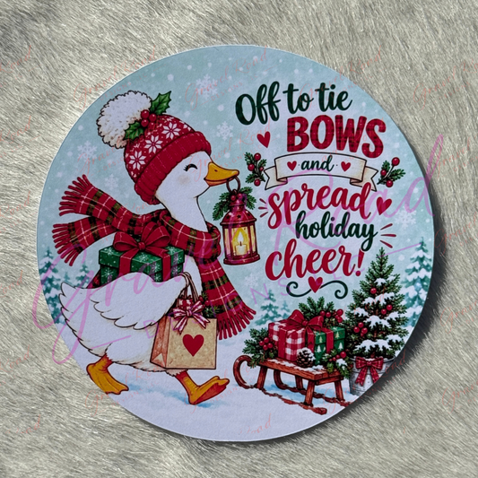 A white duck wearing a red winter hat with a pom‑pom and a red plaid scarf walks through a snowy forest carrying a wrapped gift, a heart‑decorated shopping bag, and a glowing lantern. Snow‑covered evergreen trees and a sled full of presents sit in the background. The illustration includes the phrase “Off to tie bows and spread holiday cheer!” adding to the festive, cozy holiday theme. Displayed on a faux fur background.