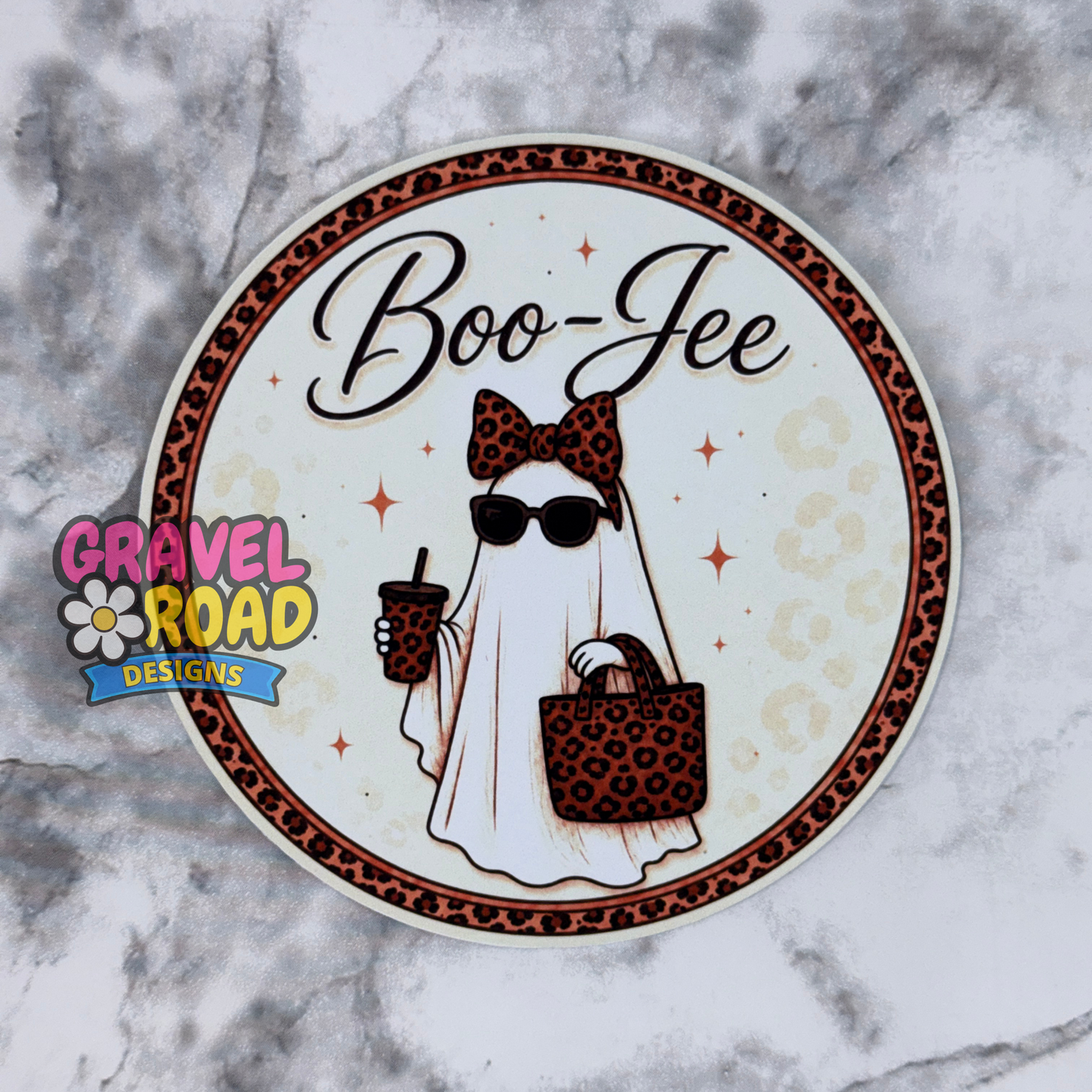 A circular cardstock featuring a ghostly figure in a leopard-print bow, sunglasses, and tote bag, holding a drink. The pin has a cream background with a brown leopard print border and the text 'Boo-Jee' in black script. Gravel Roads Designs watermark appears on the left hand side.
