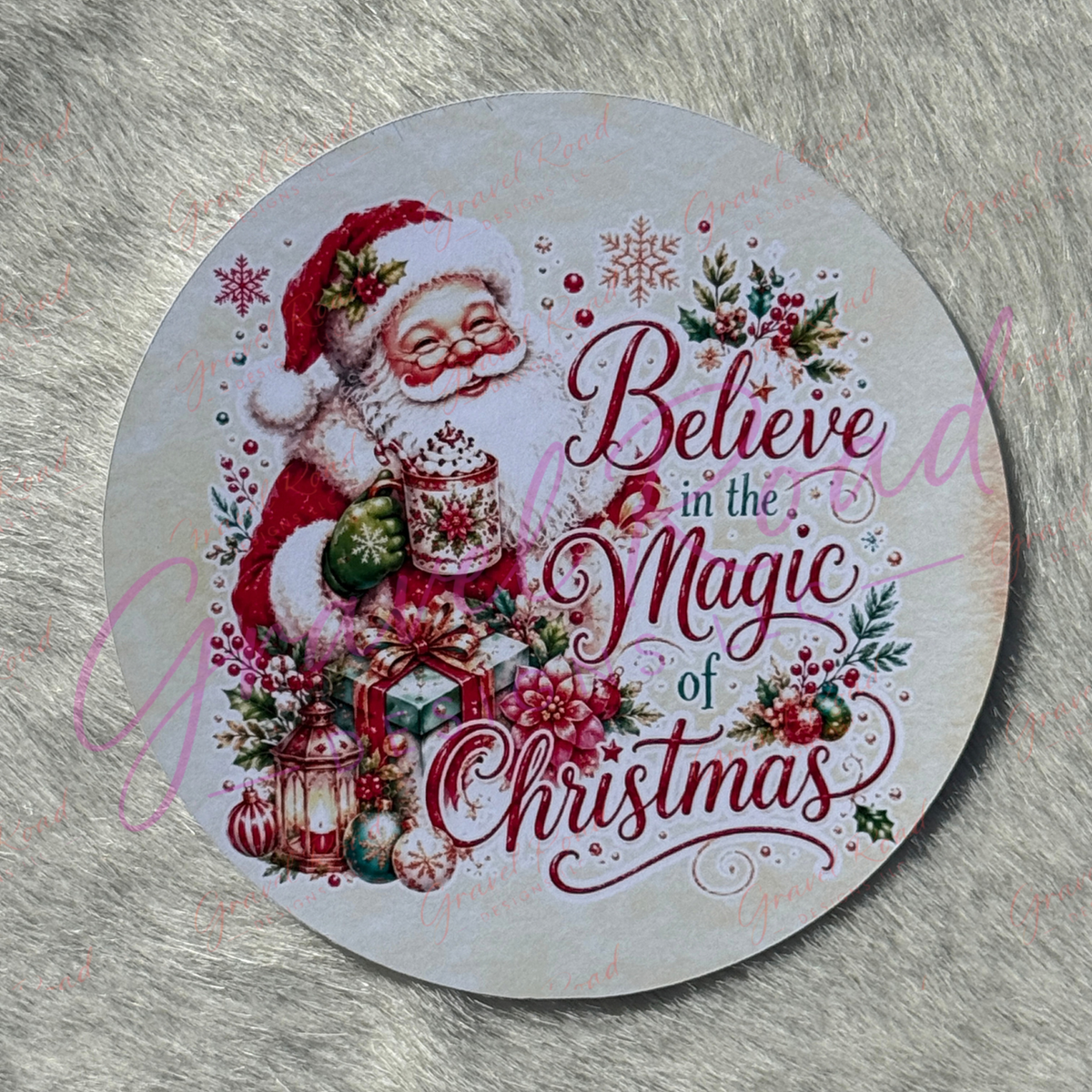 A Christmas cardstock of Santa Claus holding a holiday‑themed mug, surrounded by wrapped gifts, ornaments, holly, berries, lanterns, and snowflakes, with the phrase “Believe in the Magic of Christmas” displayed across the design. Displayed on a faux fur background.