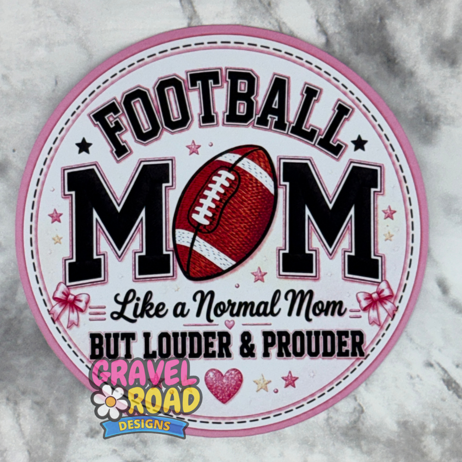 A circular cardstock design with a pink border and the text 'FOOTBALL MOM Like a Normal Mom BUT LOUDER & PROUDER,' featuring a football graphic and the Gravel Road Designs logo at the bottom, shown on a gray marble surface.