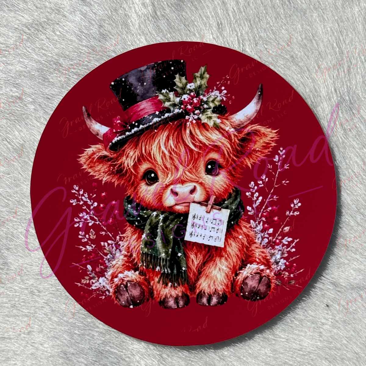 A round cardstock featuring a festive illustration of a shaggy red Highland cow wearing a black top hat with red ribbon and green holly, a dark green scarf, and holding a piece of sheet music. The cardstock is displayed on a textured gray background.