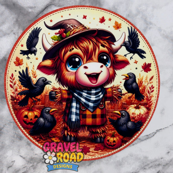 A circular Halloween-themed cardstock featuring a cute fluffy brown cow, dressed as a scarecrow, wearing a witch hat and plaid scarf, surrounded by black crows, pumpkins, autumn leaves, and a cream background. The design is branded with the text 'Gravel Road Designs' at the bottom.