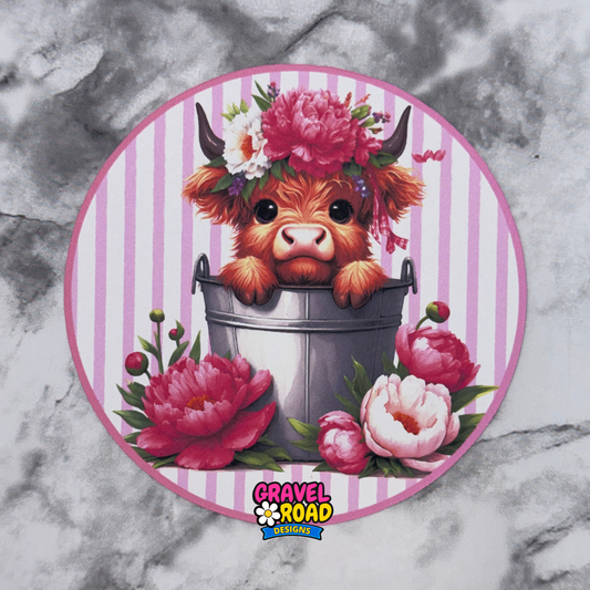 Circular design with a cartoon cow in a bucket surrounded by flowers on a marble background