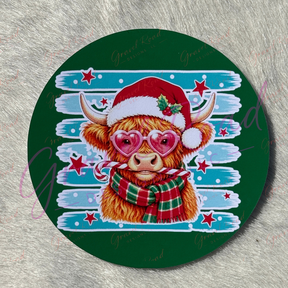 A round cardstock featuring a festive illustration of a Highland cow wearing a red Santa hat and a red, green, and white plaid scarf, set against a blue and white striped background with red stars, all on a dark green circular base.