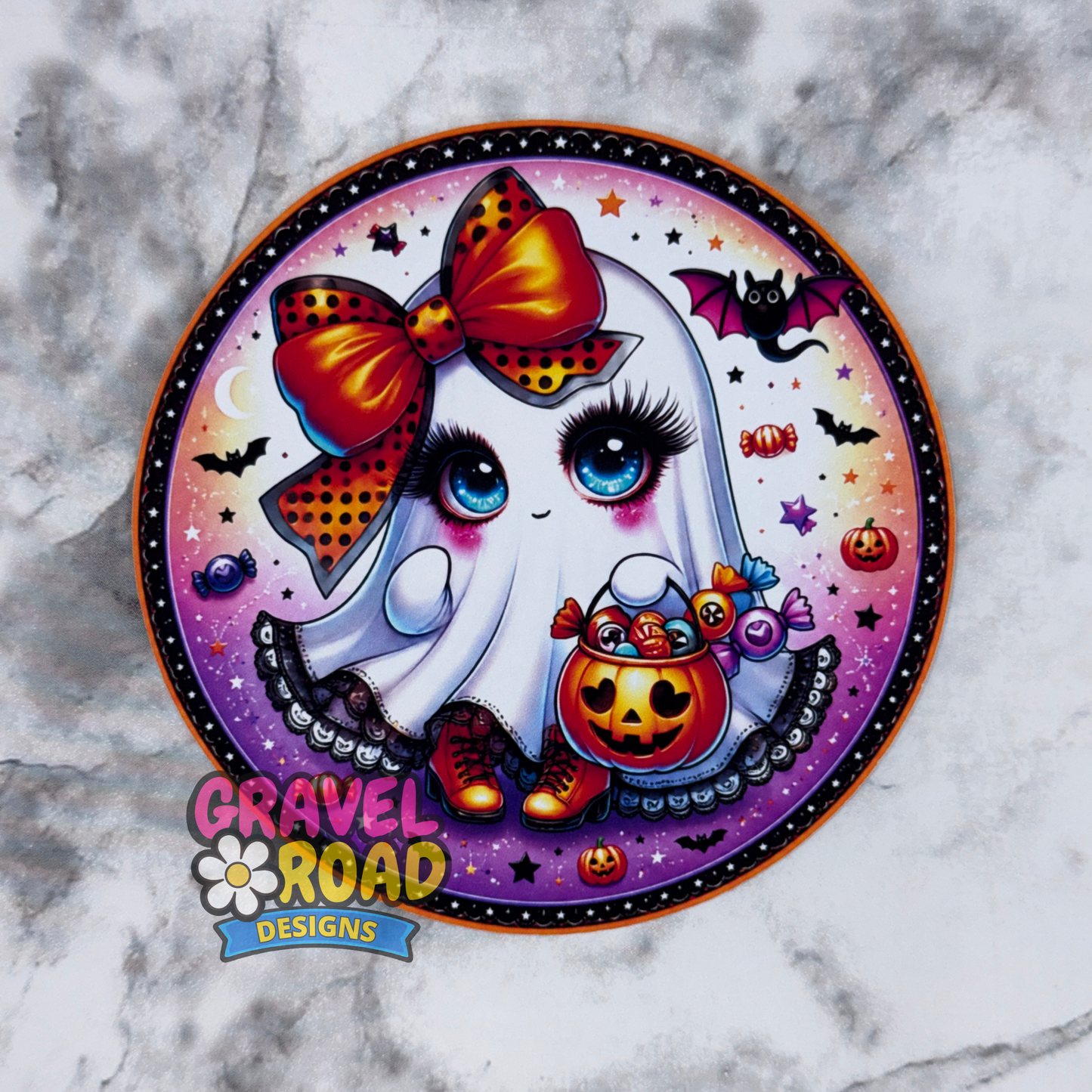 A circular Halloween-themed cardstock featuring a cute cartoon ghost with a large red and orange bow, blue eyes, and a pumpkin bucket, shown on a marble background with the Gravel Road Designs logo at the bottom.