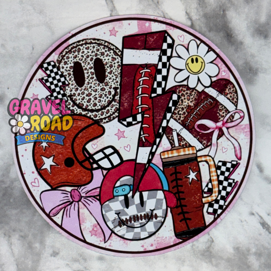 A round cardstock featuring a hand-drawn collage of sports-themed illustrations, including football, a daisy with a smiley face, checkered patterns, and pink bows. The design is branded with 'Gravel Road Designs' logo on the left side.