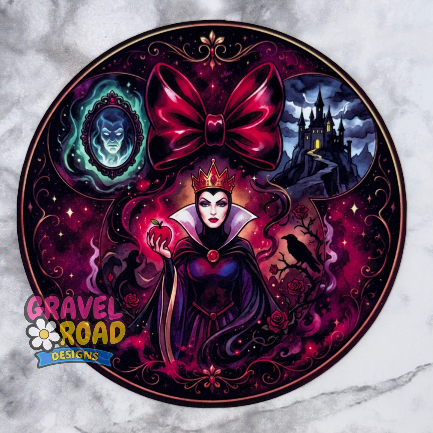 A circular cardstock featuring a dark fantasy illustration of a Queen-like character in a purple gown with a large magenta bow above her head, surrounded by gothic motifs including a castle, a blue mirror portrait, a crow, and an apple. The design is shown on a light marble-like background, with the logo 'GRAVEL ROAD DESIGNS' in the lower-left corner.